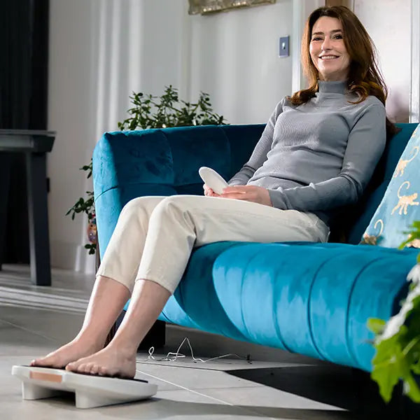 Woman relaxing on a teal sofa with her feet on PainGone Fllow